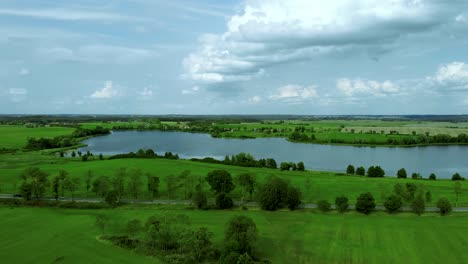 aerial footage over lake, beautiful day near grass field nad road nad pond, high trees and sky with cloud