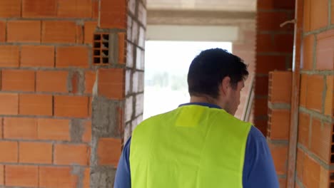 4k imágenes de un trabajador de la construcción caminando a través de un estrecho corredor dentro de una casa, rodeado de paredes de ladrillo naranja sin terminar, capturado con un gimbal siguiéndolo por detrás.