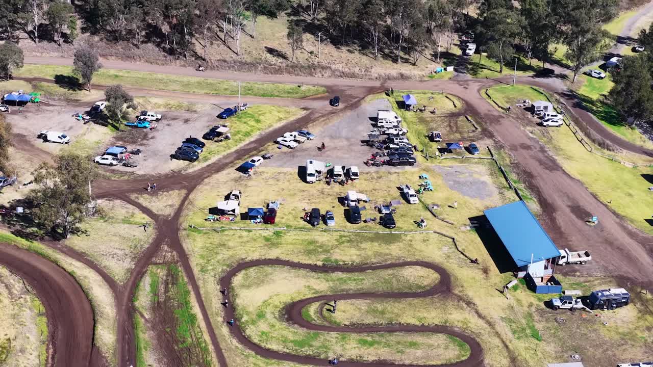 Droneoptagelser fra høj vinkel viser en buet jordracerbane med køretøjer og tilskuere i nærheden.