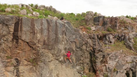 Un-Hombre-Está-Escalando-Una-Montaña,-Mientras-Que-Una-Mujer-Lo-Espera-En-La-Cima