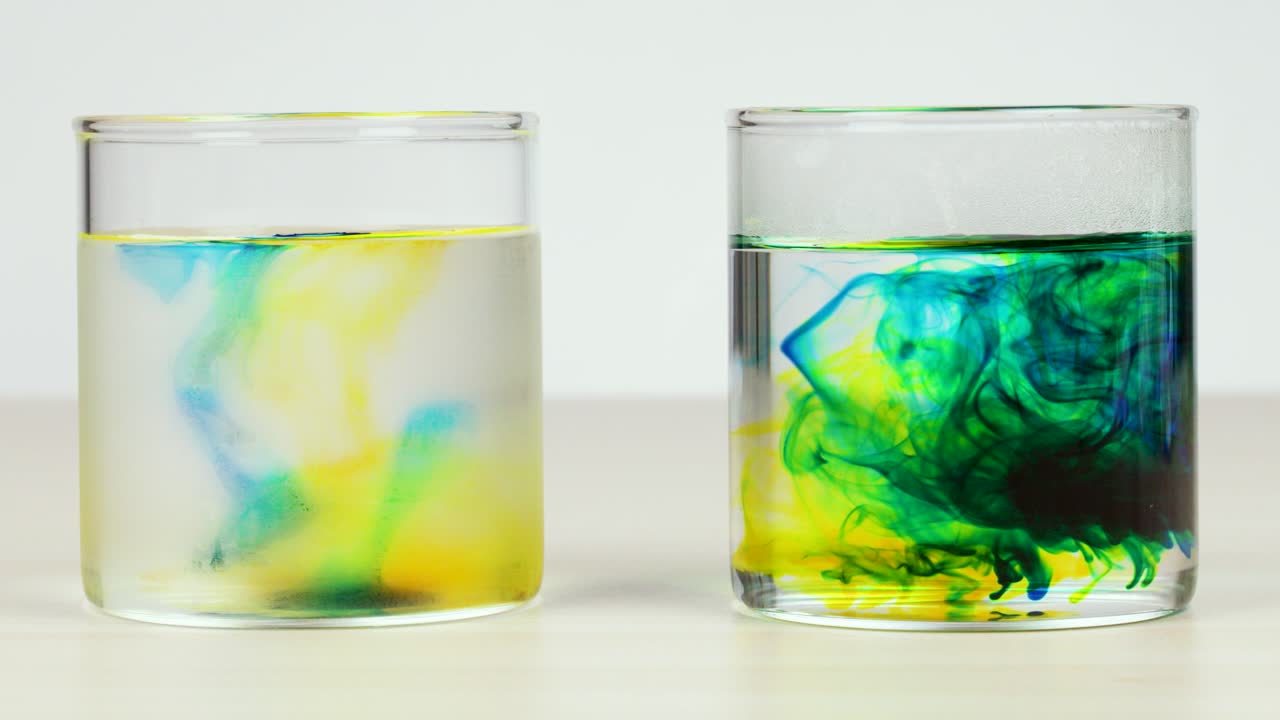 Yellow and blue food coloring disperses in clear water, demonstrating diffusion rates in glass containers
