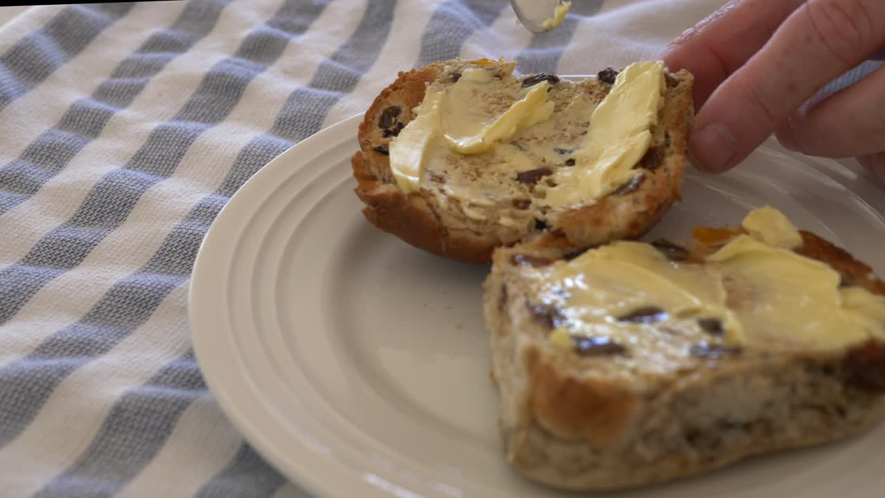 Slow motion pan into hot cross buns on a plate being buttered with kitchen knife during Easter
