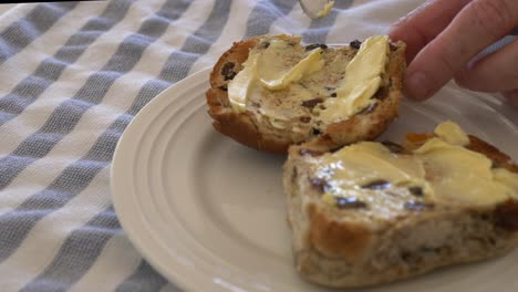 Slow-motion-pan-into-hot-cross-buns-on-a-plate-being-buttered-with-kitchen-knife-during-Easter