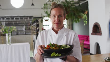 caucasian female chef preparing a dish and smiling in a kitchen