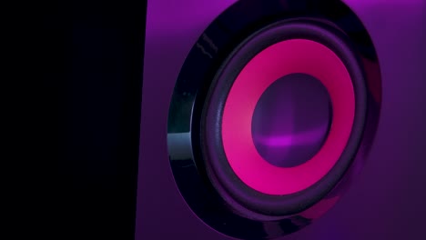 audio speakers lit by colorful neon club lights. professional studio subwoofer speaker isolated. concept for dance music party. close up. slow motion