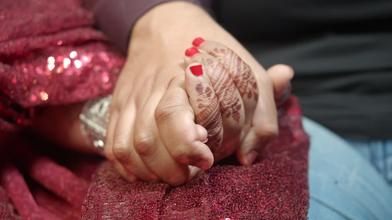 Coppia che si tiene per mano con Mehendi e abiti rossi
