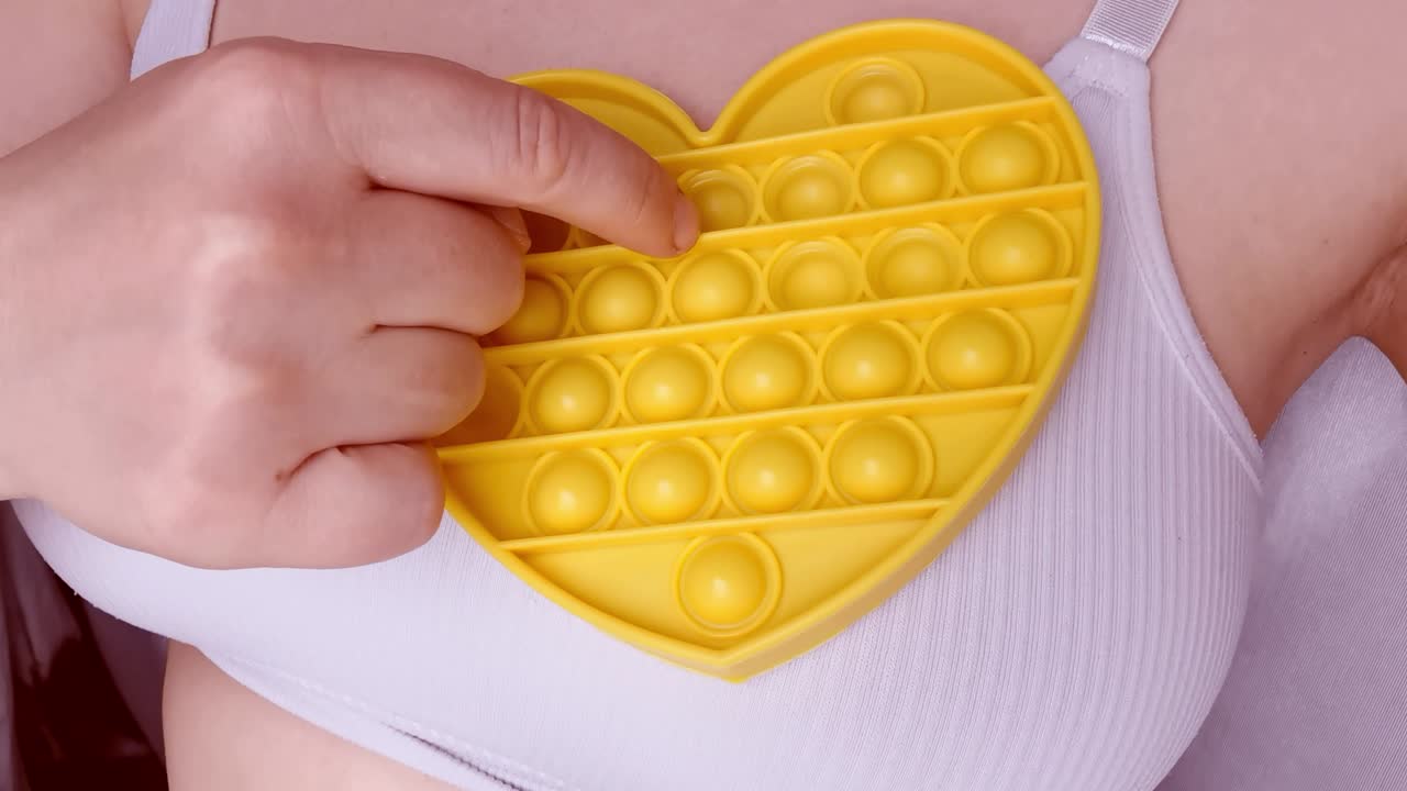 nuevo juguete para bebés. pop it juego de dedos. color gracioso. mano adulta apretando silicona redonda. cambio de forma. forma de corazón amarillo