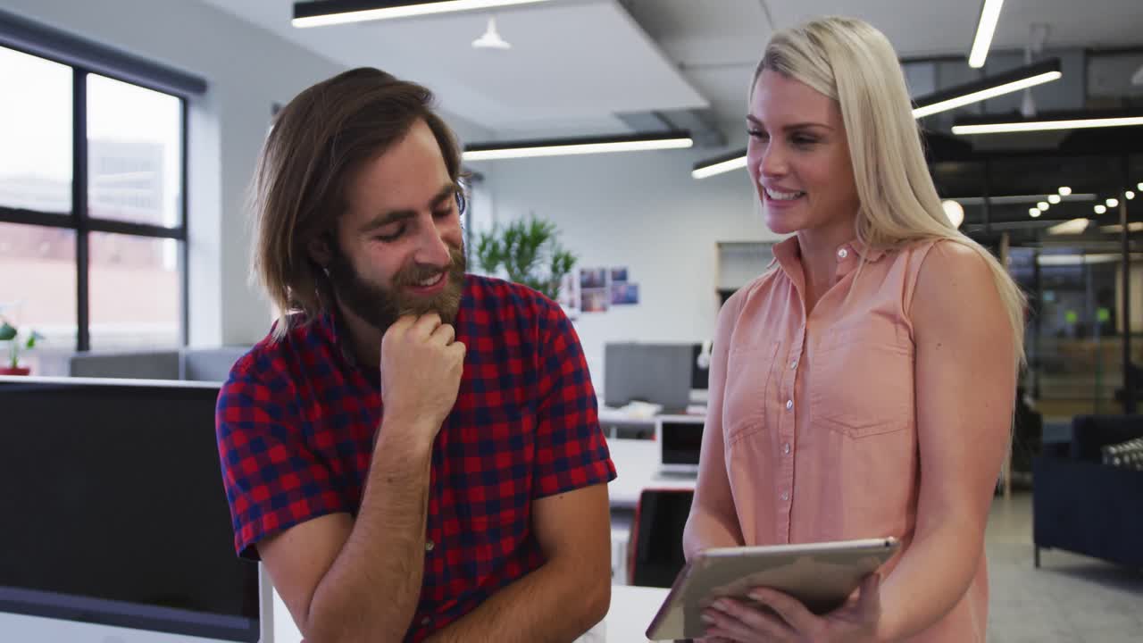 gente de negocios caucásica usando tableta digital hablando y sonriendo en una oficina moderna