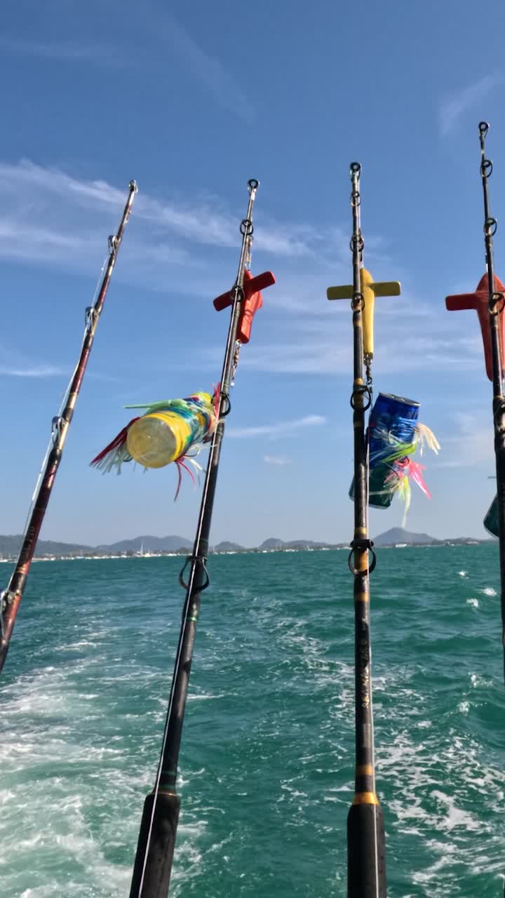 Canne da pesca ondeggiano su una barca in movimento sotto un cielo limpido a Phuket, Thailandia. L'oceano vivace e le bandiere creano una scena dinamica.