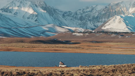 remote wild camping on shore of valley lake with snowy mountains, aerial