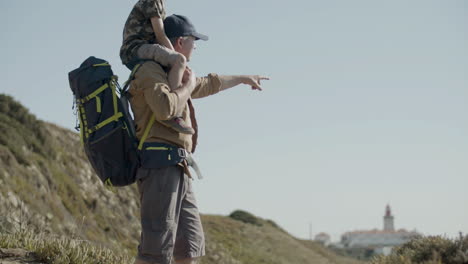 tracking shot of father carrying his son on shoulders while hiking in mountains