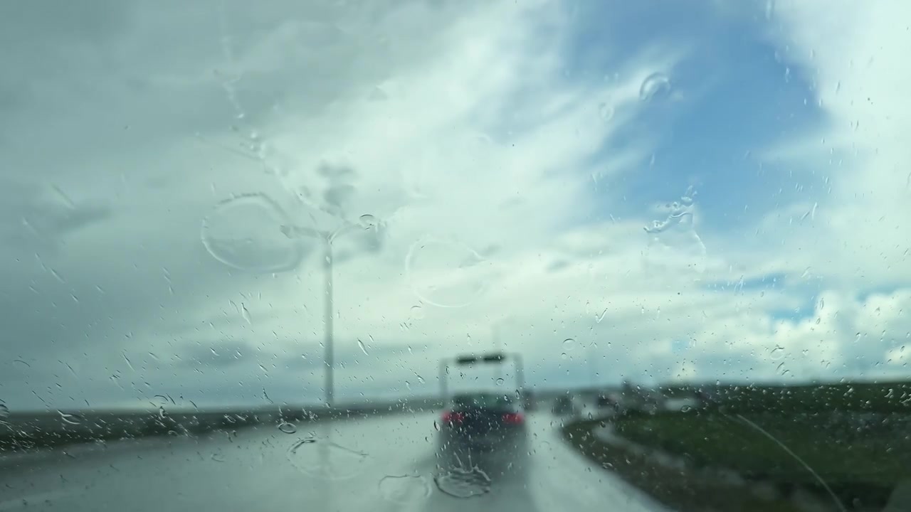 Guida su strada sotto la pioggia con vista di veicoli sfocati e cielo nuvoloso in lontananza nel tardo pomeriggio