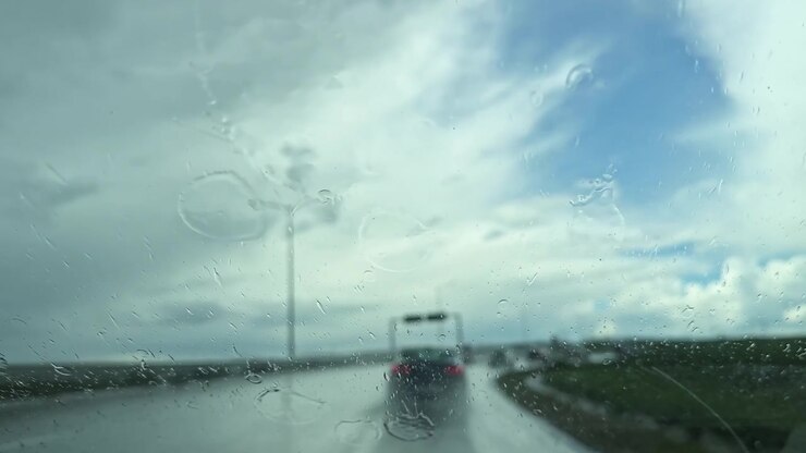 Guida su strada sotto la pioggia con vista di veicoli sfocati e cielo nuvoloso in lontananza nel tardo pomeriggio