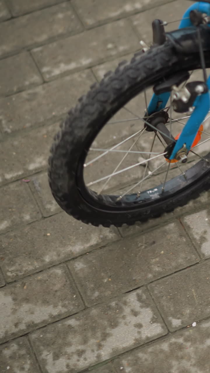 자전거 에 서있는 아이의 아래쪽 시선, 자전거를 조심스럽게 타고, 아이는 젠 쇼트와 다채로운 샌달을 입고, 자전기에는 파란색 앞 바가 있습니다.