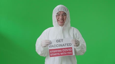 asian man wearing personal protective equipment uniform ppe and holding get vaccinated stopping covid starts with you sign in the green screen studio