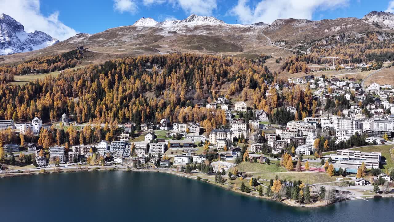 An aerial view of the exclusive resort town of St. Moritz Dorf on the shores of its lake in Kanton Graubünden, Schweiz. The town is nestled amongst golden larch forests
