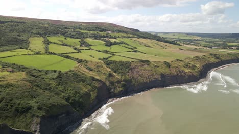 Aerial-drone-shot-of-North-Yorkshire-coastline-near-Ravenscar-with-green-fields-and-ocean