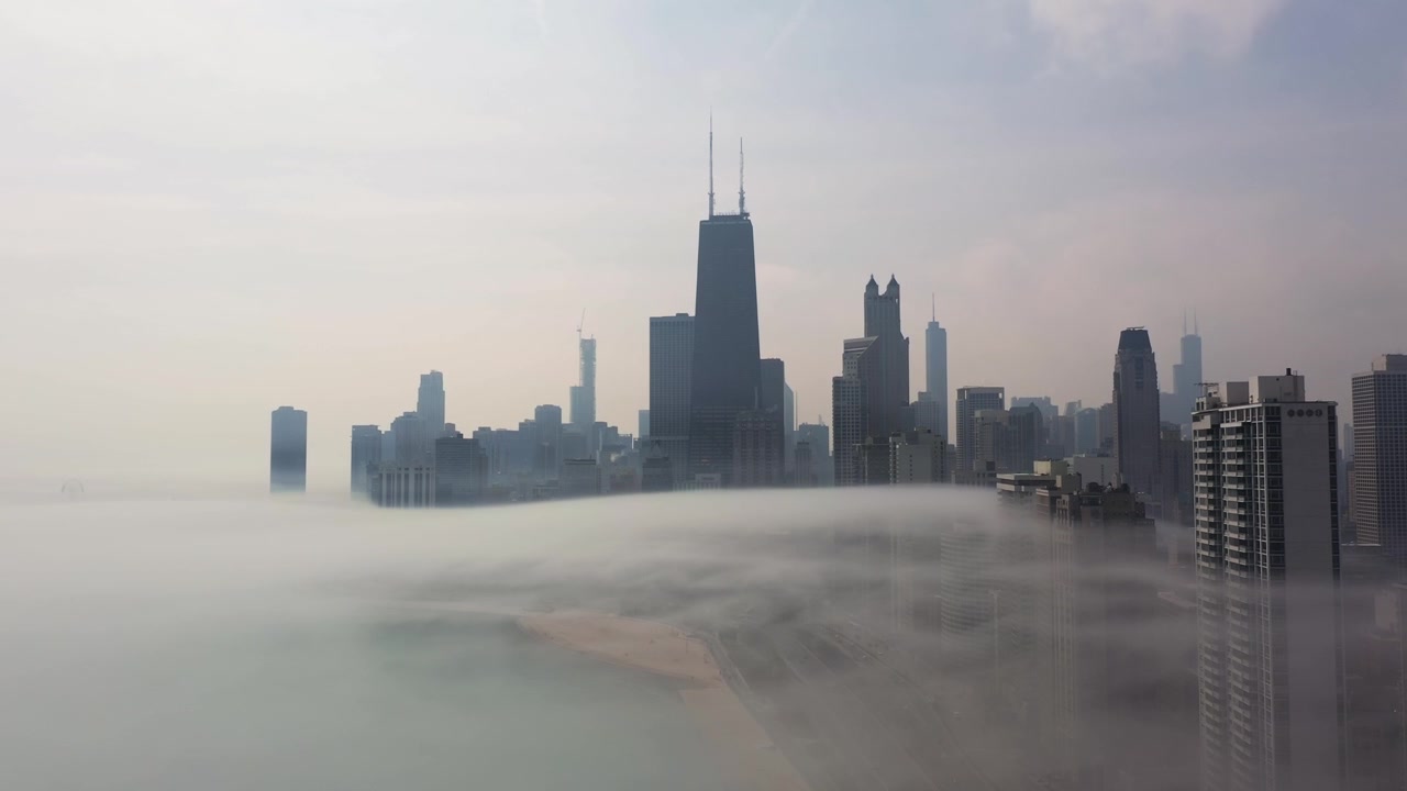 Riprese aeree fluide si innalzano da una fitta nebbia mattutina per rivelare i grattacieli di Chicago che emergono sopra la foschia, creando una vista urbana atmosferica e drammatica.