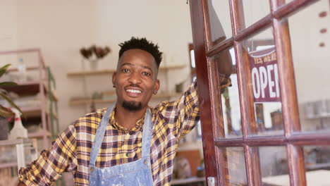 happy african american male potter standing in shop entrance and smiling, slow motion