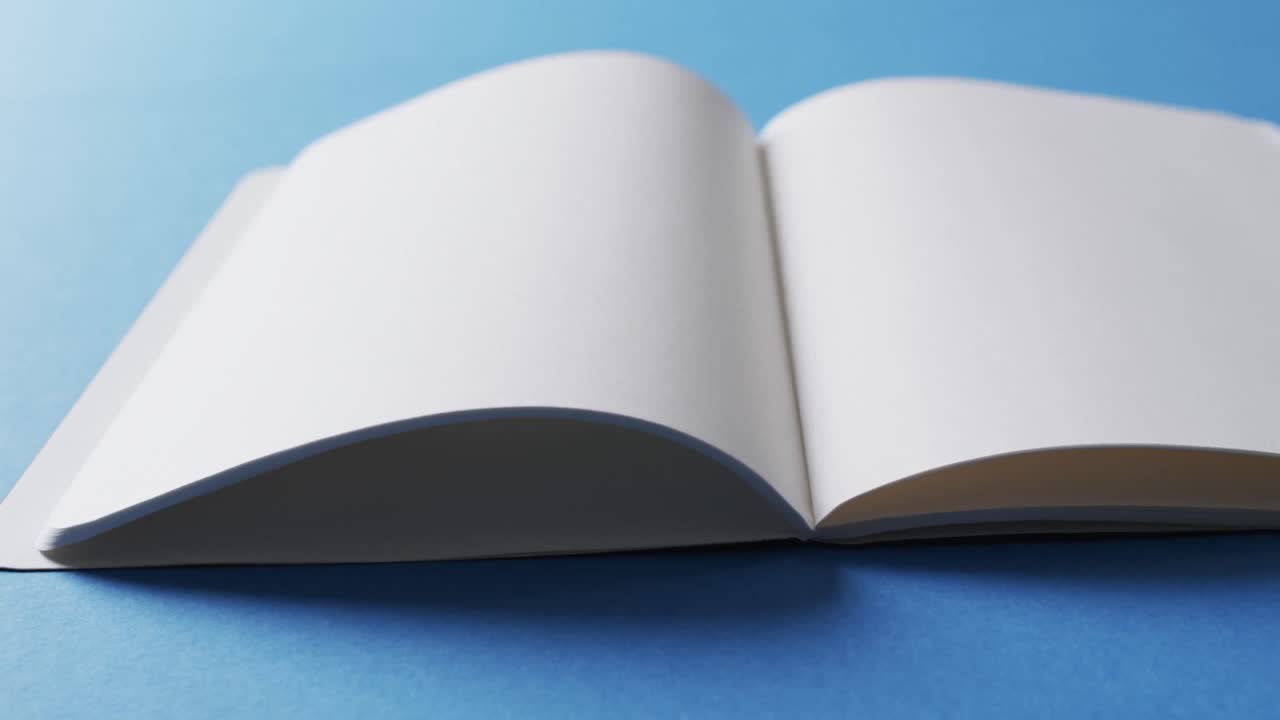 Close up of open blank book with copy space on blue background in slow motion