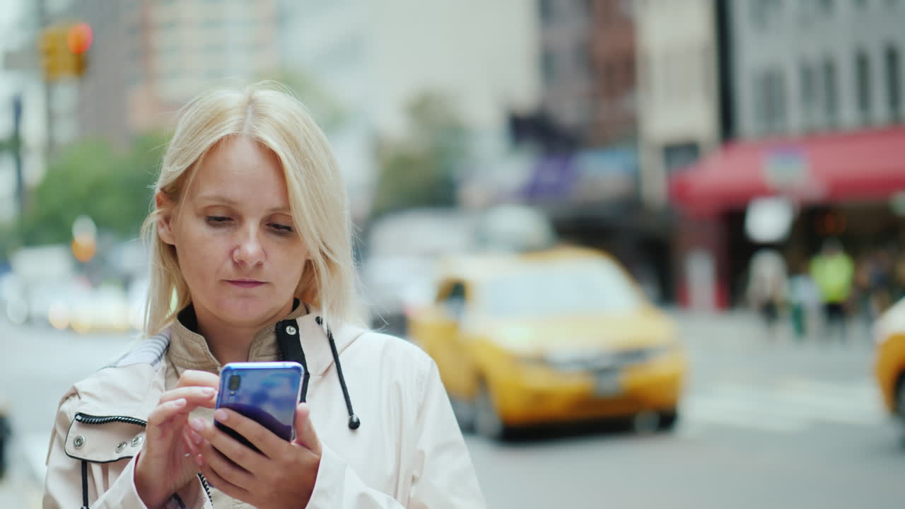 молодая женщина пользуется смартфоном на фоне офисных зданий в центре манхэттена, новый год