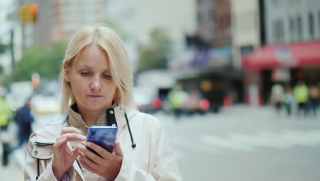 A-Young-Woman-Uses-A-Smartphone-Against-The-Backdrop-Of-Office-Buildings-In-Downtown-Manhattan-New-Y