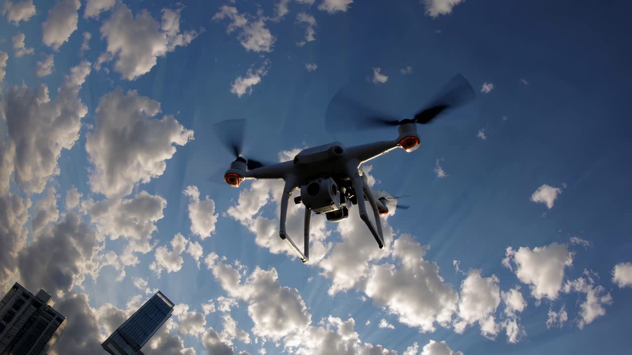 Low-angle shot of a drone flying against a vibrant sky with scattered clouds, capturing dynamic