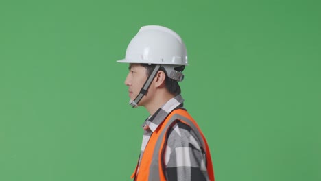 close up of side view asian male engineer with safety helmet waving hand while walking in the green screen background studio