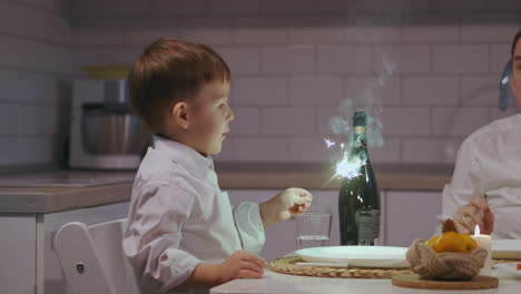 un niño sostiene y mira con alegría a una chispa sentado en la cena en la víspera de navidad. celebrar el año nuevo con chispas. niño 3-5 sostiene un fuego chispa. imágenes de alta calidad 4k