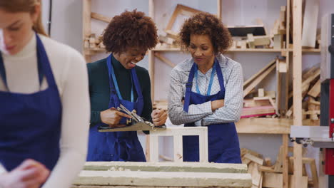 tutor with female carpentry student in workshop studying for apprenticeship at college