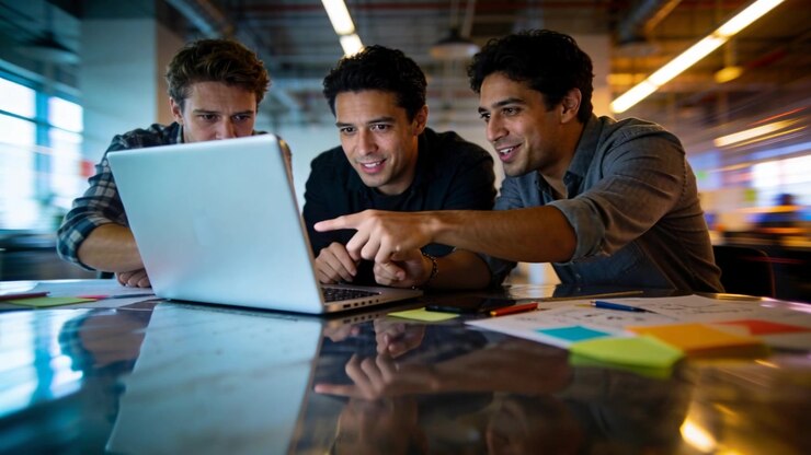 Leaning three coworkers working on task on laptop in office wearing shirts pointing at sticky notes