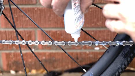 primer plano de un mecánico que coloca lubricante en una cadena de bicicleta recién limpiada como parte del mantenimiento de rutina