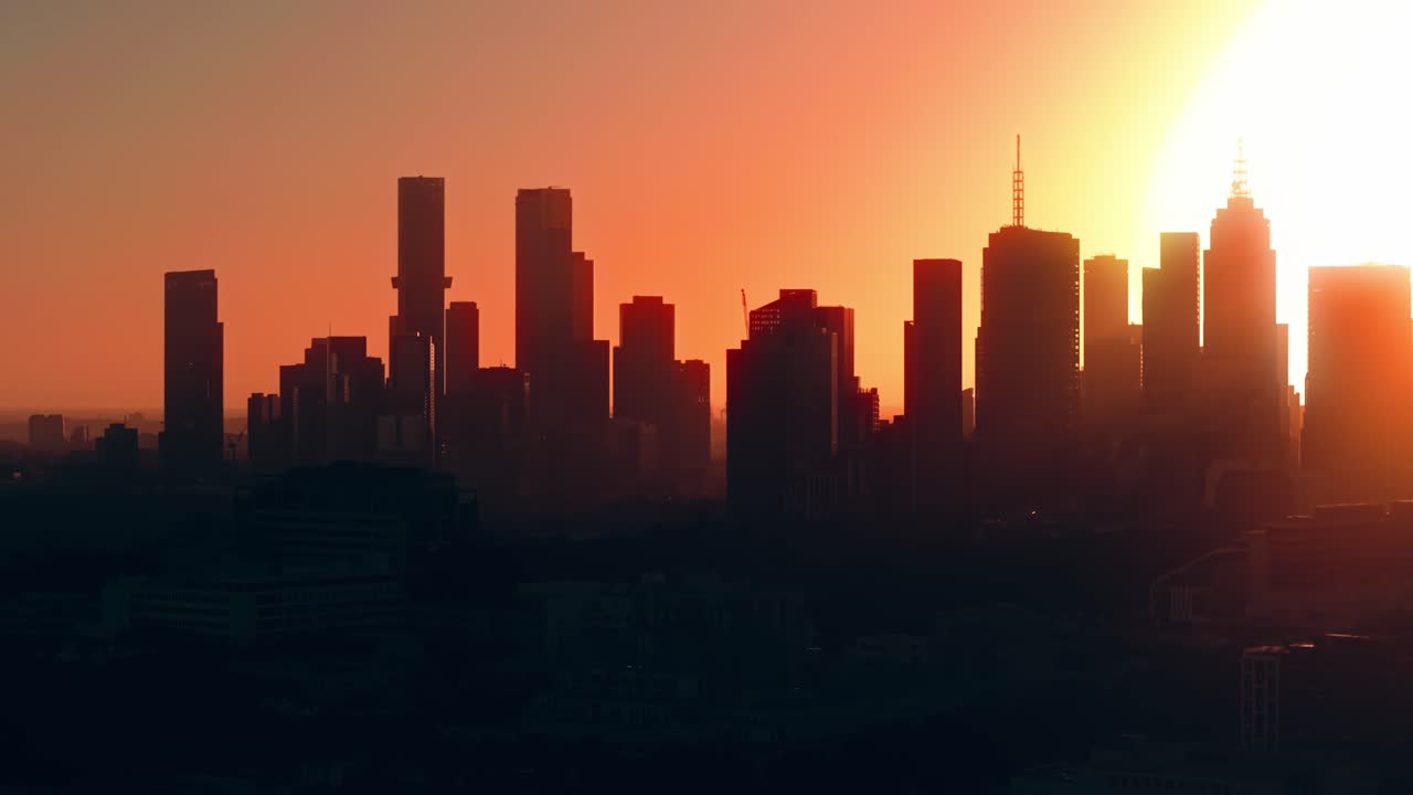 Horizonte de la ciudad de Melbourne al atardecer con el sol destellando entre rascacielos, toma aérea de establecimiento con un telón de fondo metropolitano medio.