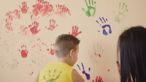 un niño lindo feliz y su joven madre se están divirtiendo dejando sus coloridas huellas de manos en la pared.