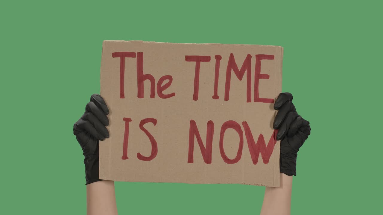 руки неизвестного человека в черных перчатках поднимают картонный плакат время сейчас. равенство и единство концепция. изолированный зеленый экран, хроматический ключ. близко. замедленное движение