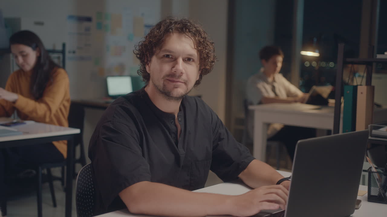 Man Using Laptop and Posing on Camera in Office at Night