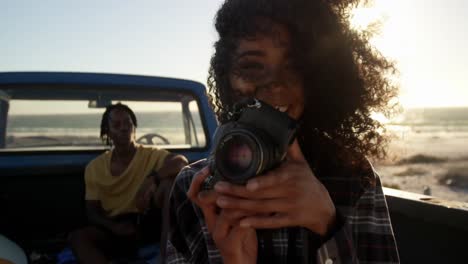 mujer tomando fotos con una cámara digital en una camioneta en la playa 4k