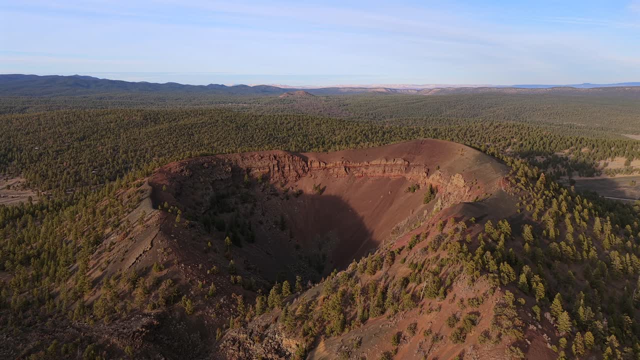 Una drammatica prospettiva da drone di un vulcano spento a cono di scorie, che rivela un cratere profondo e alberato. Questa ripresa in 4K evidenzia l'imponente scala geologica di una remota natura selvaggia vulcanica.