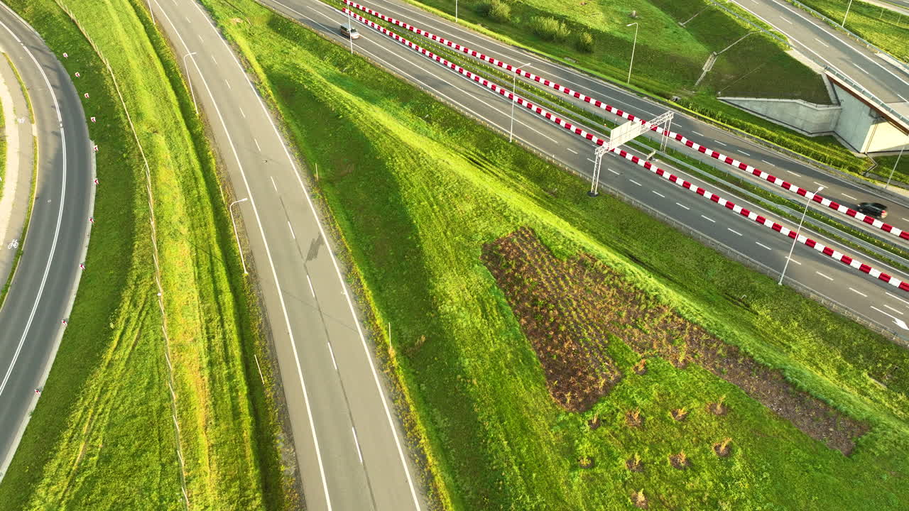 Extreme close aerial view of cars and vans driving on a multi-lane highway (S6) with distinctive red and white barriers, flanked by steep green embankments