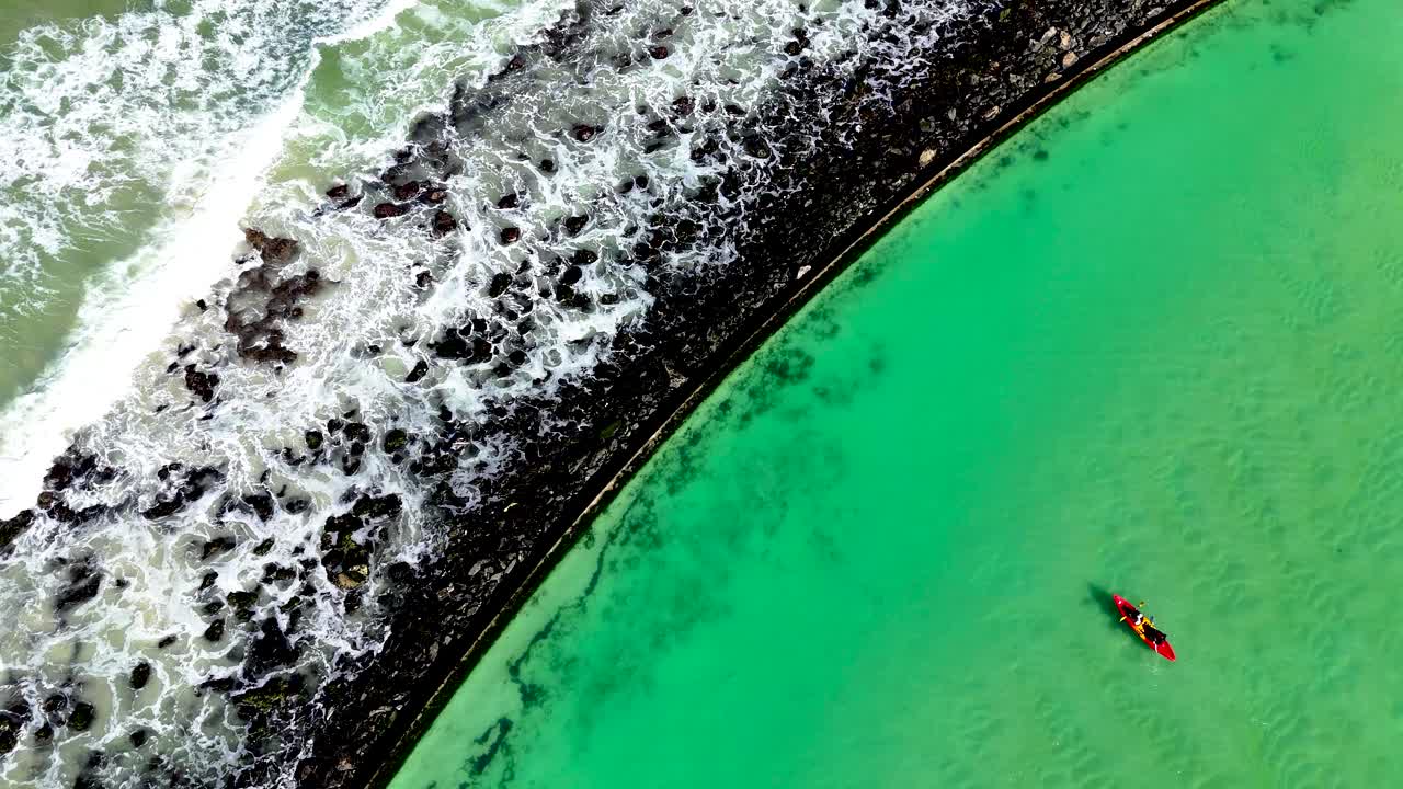 Aerial clip of canoeists in a tidal pool with the waves breaking onto rocks on the ocean side