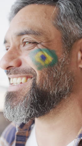 video vertical de un hombre biracial feliz con la bandera de brasil en la mejilla