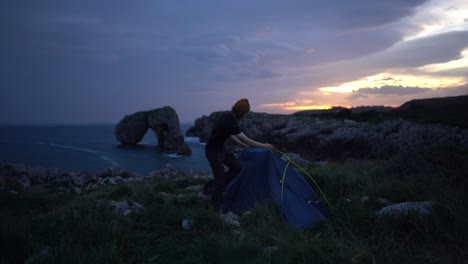 hiker man disassembling tent in nature ocean cliff campsite at sunrise