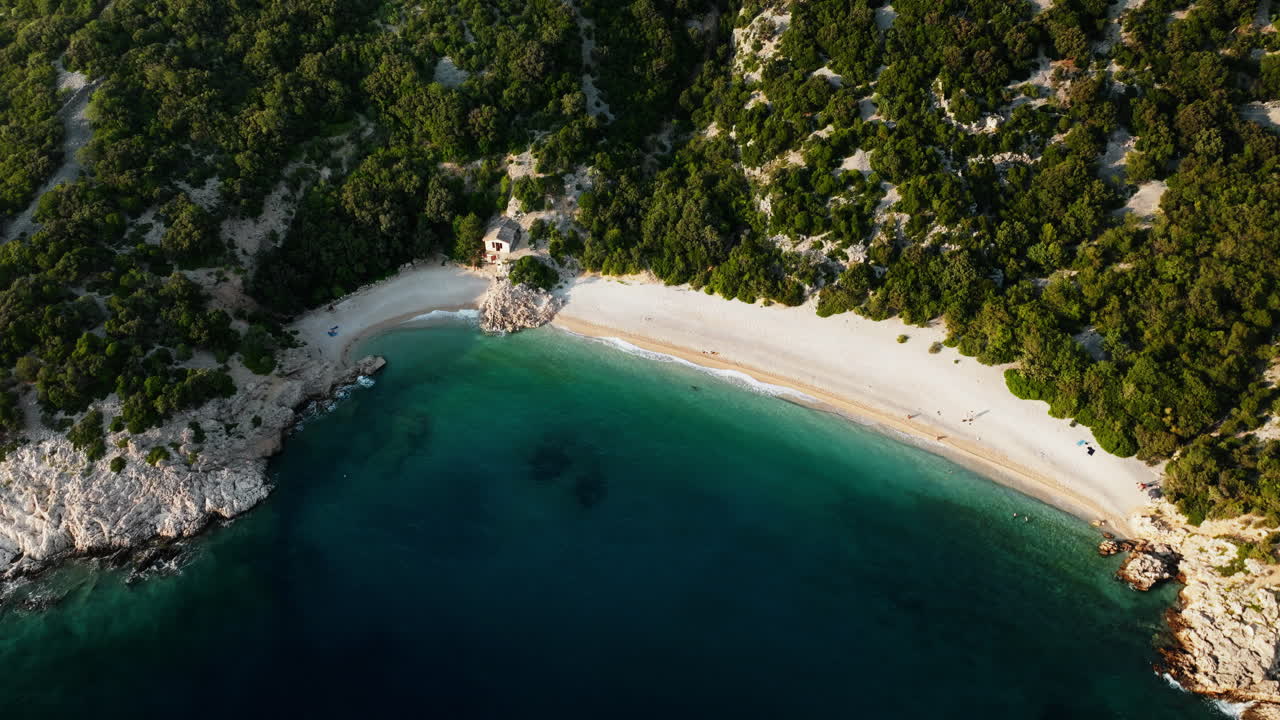 Drone oblique bird's eye view of white sand at golden hour with vibrant blue water, Lubenice beach Croatia