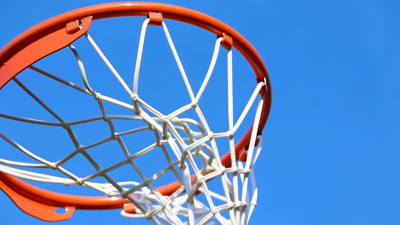 Una scena dinamica ed energica di un pallone da basket che viene lanciato nel canestro, sullo sfondo di un cielo azzurro limpido in un ambiente ricreativo all'aperto. L'anello metallico arancione e il materiale della rete aggiungono