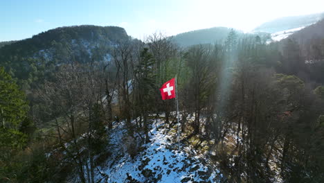 Rote-Schweizer-Fahne-Flattert-An-Einem-Sonnigen-Tag-Auf-Einem-Fahnenmast-Im-Schneebedeckten-Juragebirge