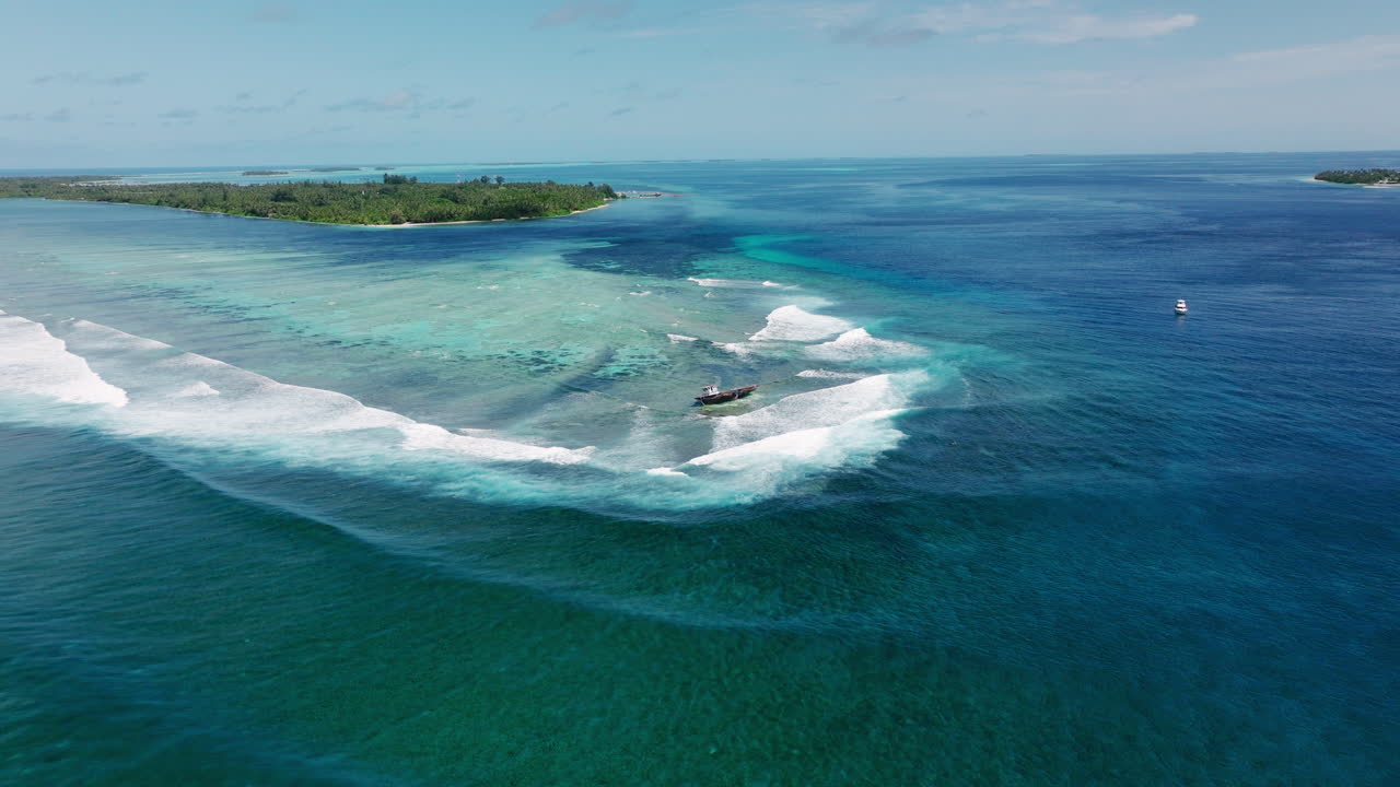 Drone panoramic aerial static of Maldives reef break with vivid blue tropical water crashing around shipwreck
