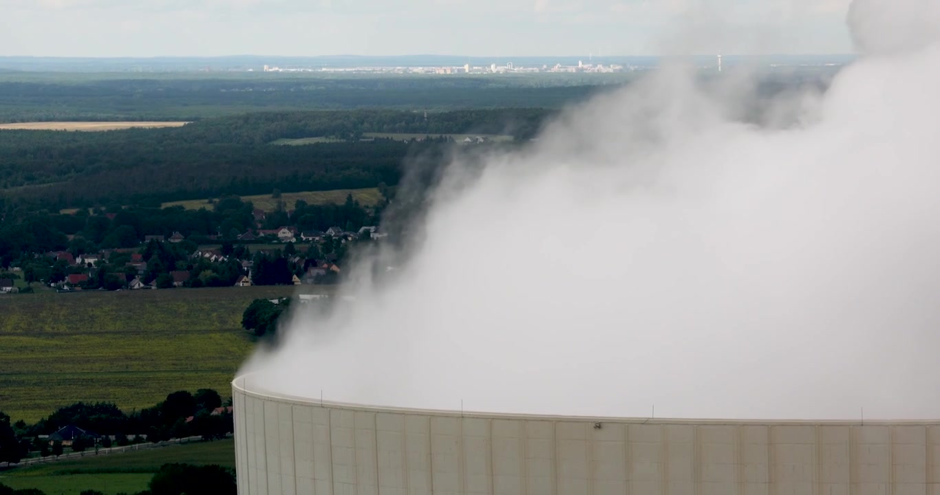Vista aproximada de vapor branco pesado de uma usina termelétrica a carvão misturando-se com nuvens de tempestade dramáticas, representando a pegada de carbono e o abandono do carvão.