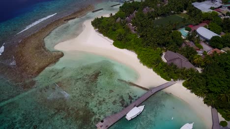 An-Island-In-Maldives---Lush-Island-On-White-Sand-With-Guesthouses,-Wooden-Walkway,-And-Boats-Docked-On-The-Shore-Surrounded-By-Aqua-Blue-Ocean-Water---Aerial-Shot