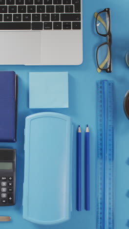 video vertical de portátil, gafas, café, plantas y papelería sobre un fondo azul