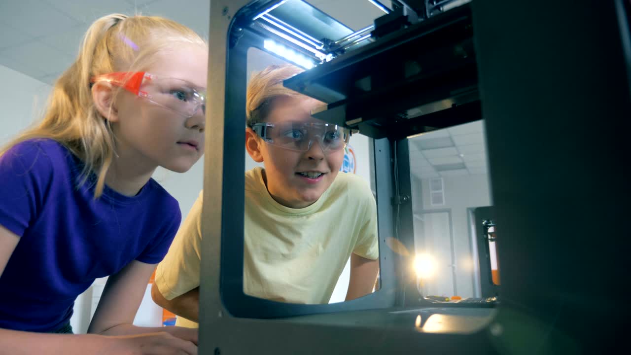un niño y una niña adolescentes están observando un mecanismo tecnológico en funcionamiento.